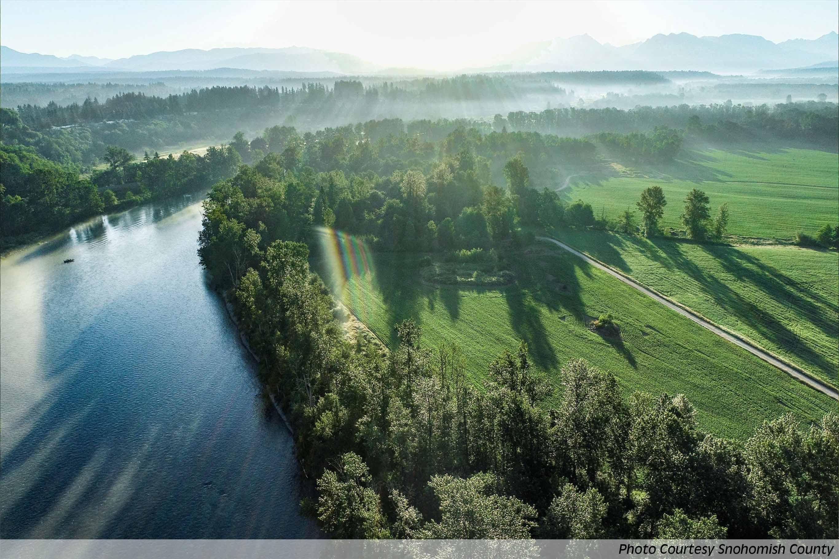 Taulco Valley - beautiful aerial of Snohomish River with sunbeams streaming across lush green farmland