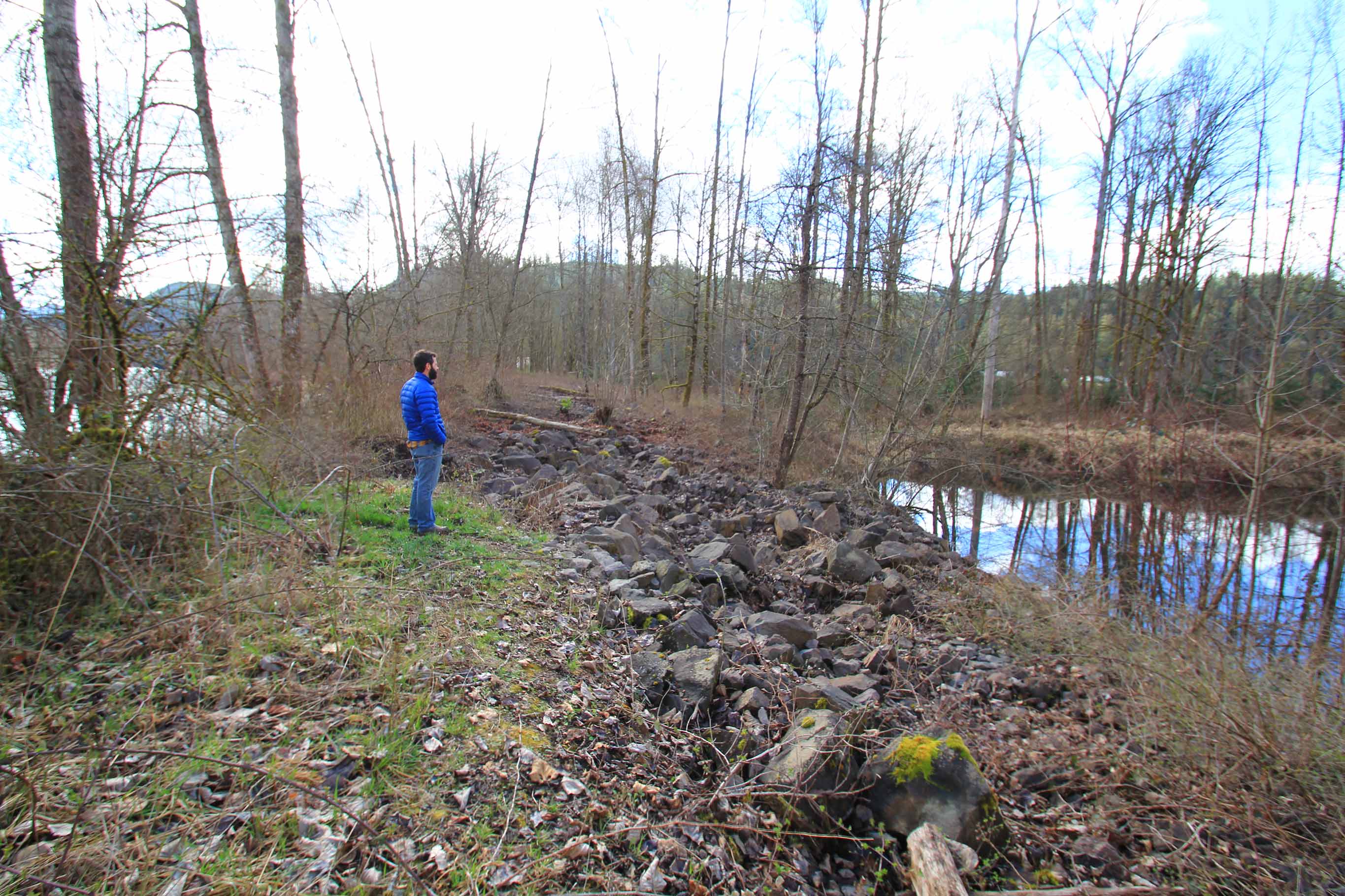 A man stands on a rocky area between the two rivers, overlooking the Tualco Valley project area
