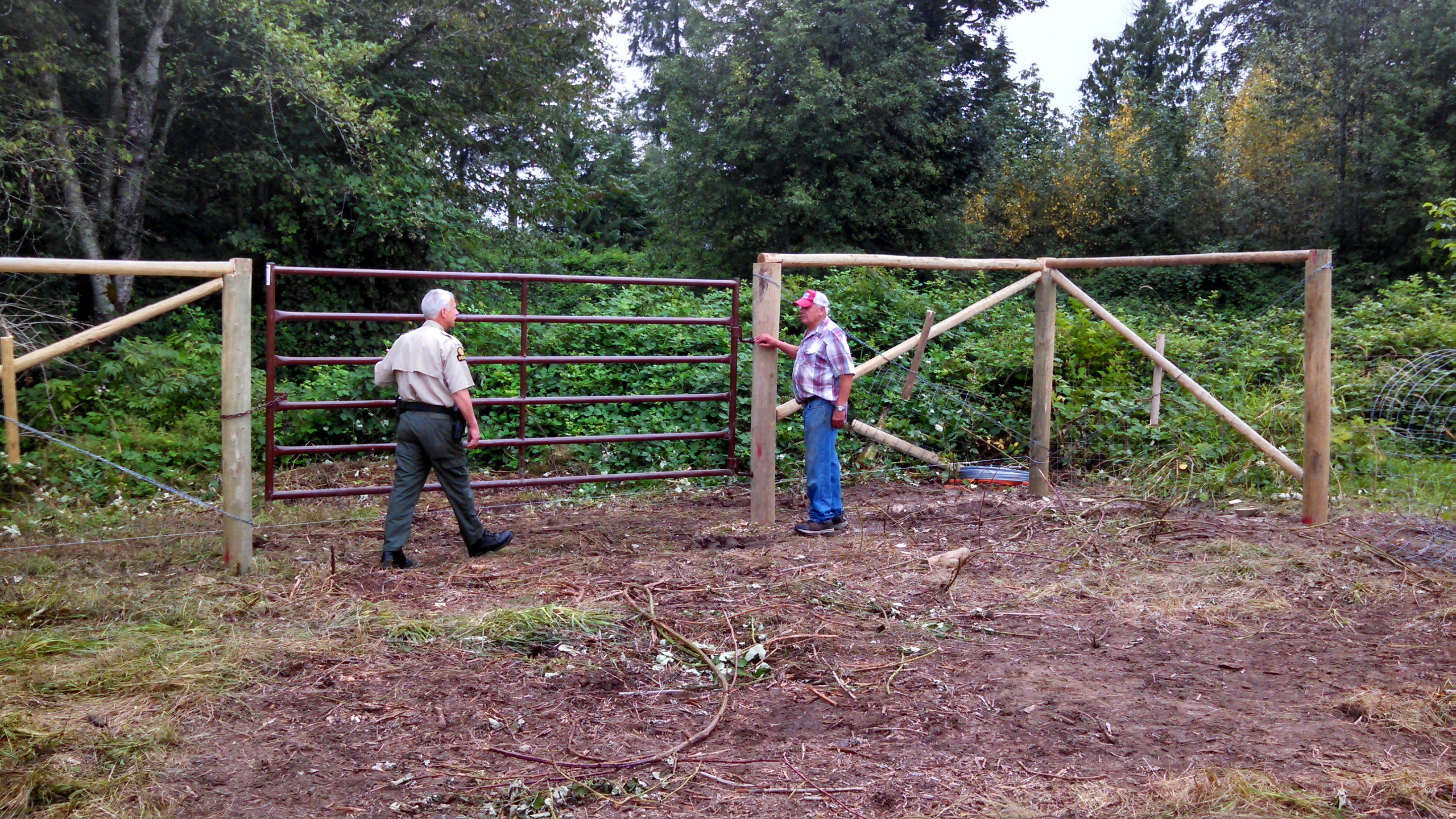 Tulalip Tribes Natural Resources Department news link to Tribes Minimize Elk Damage with Cost Effective Fence with image of two people by high fence with gate